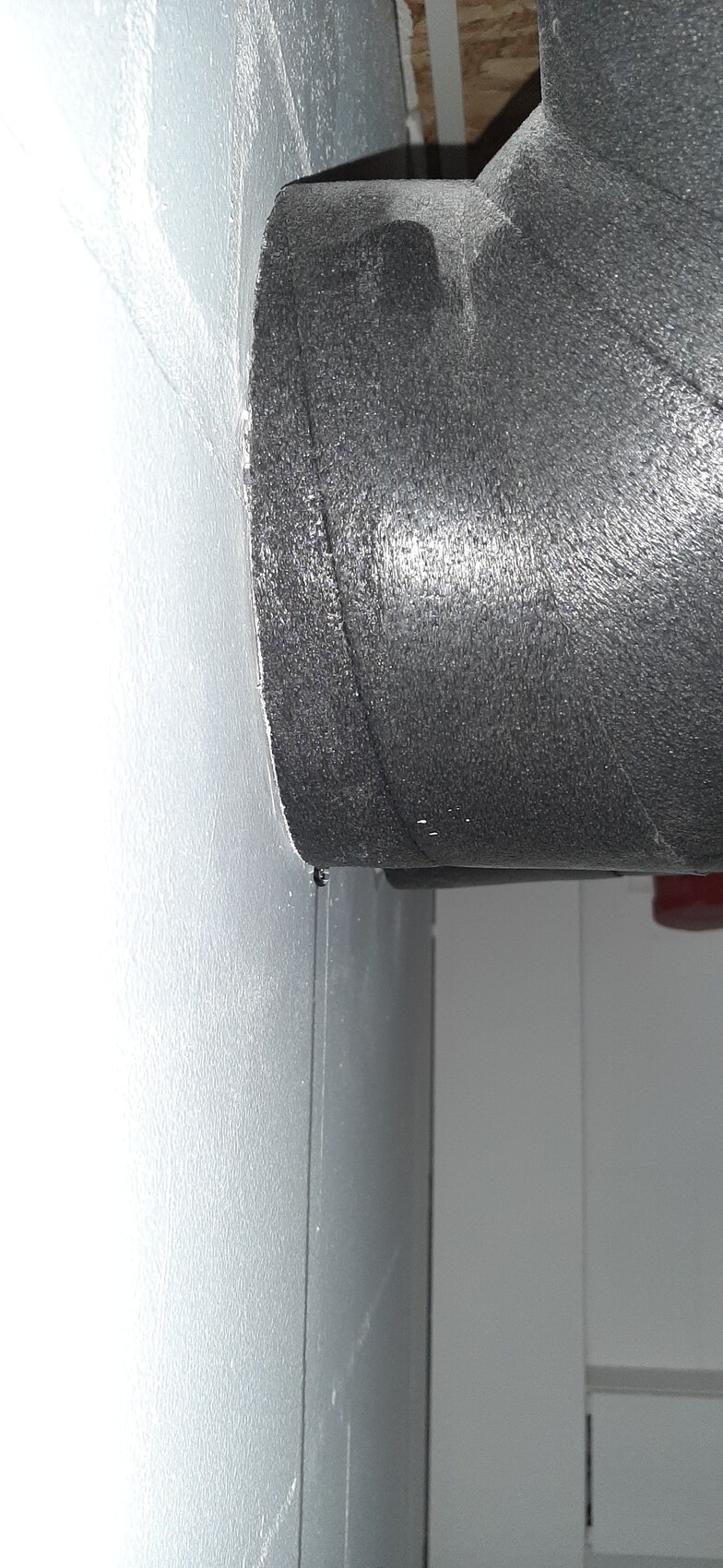 Large black roller made of coarse material in front of gray wall, close-up of machine part.
