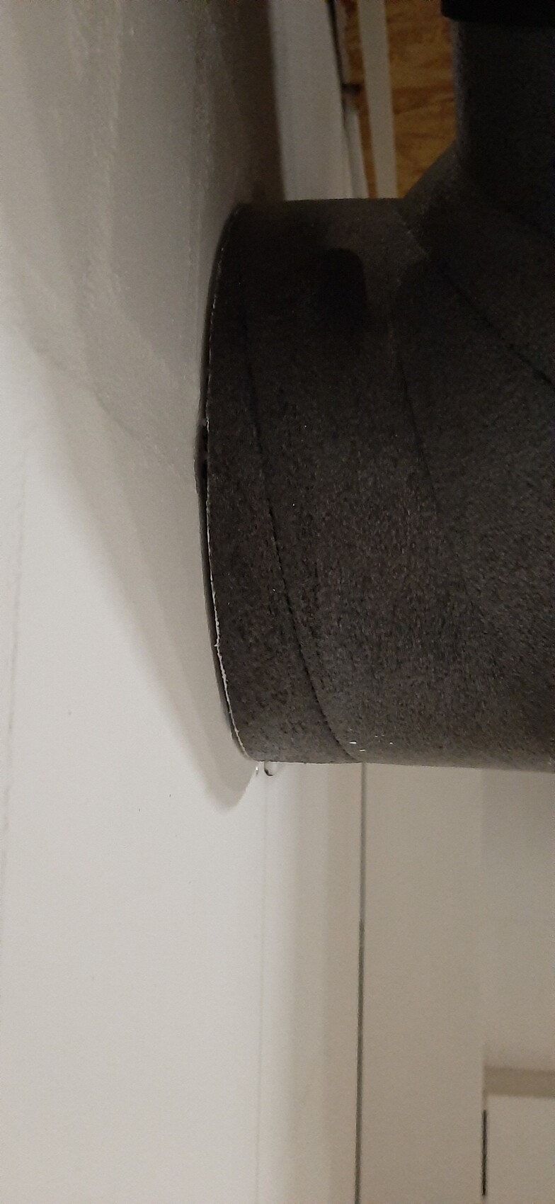 Black, padded round object on a white wall; close-up of fabric surface.