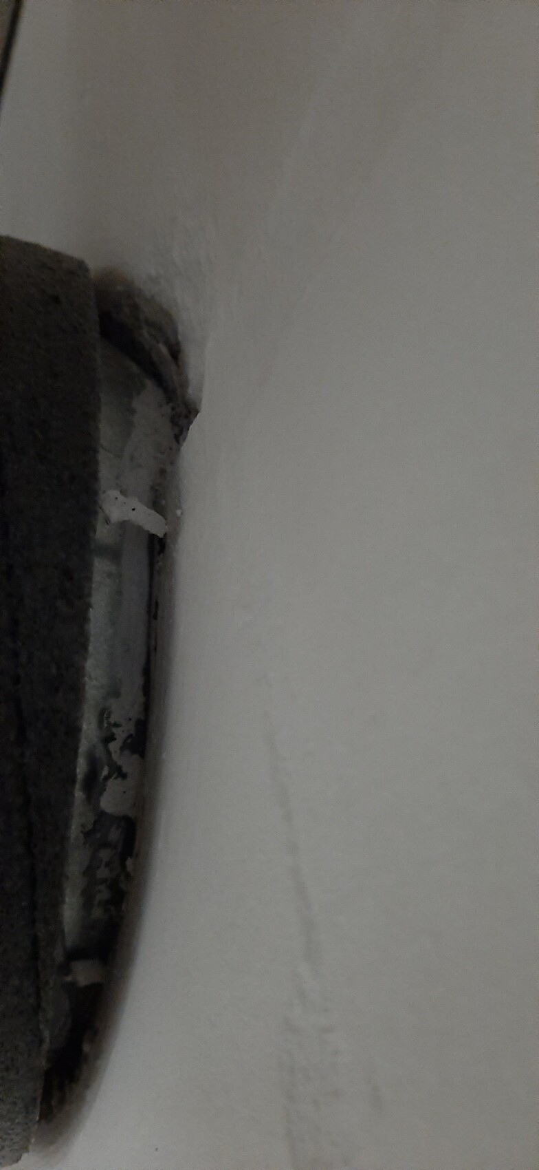 Close-up of white wall next to a dark, round metal opening on the left edge.