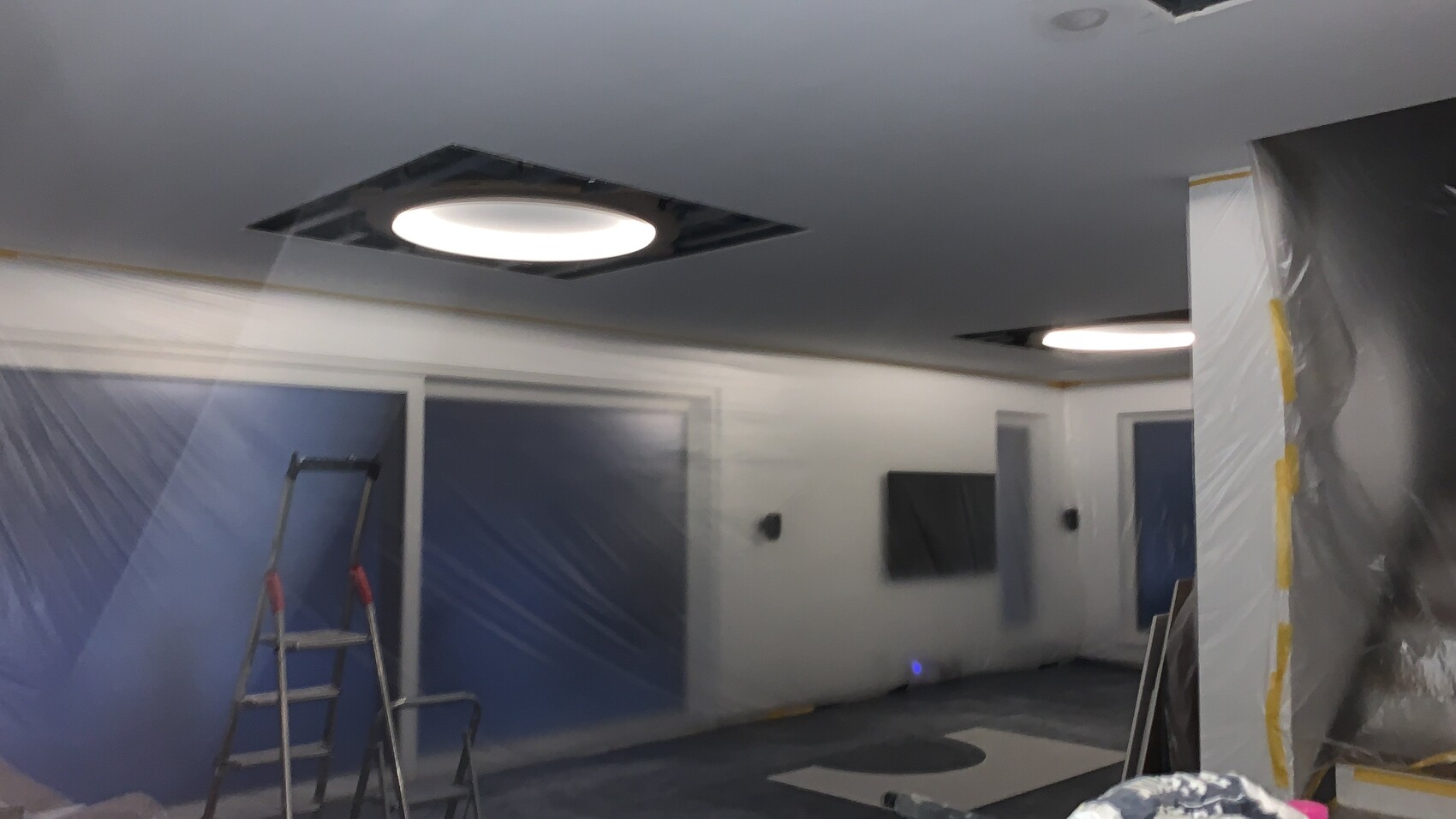 Raum unter Renovierung mit Plastikfolie an Wänden, Leiter und offenen Deckenaussparungen.