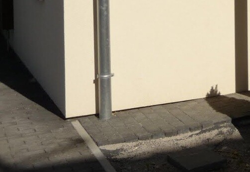 Beige building wall with vertical downpipe, paved walkway, curb and shadow.