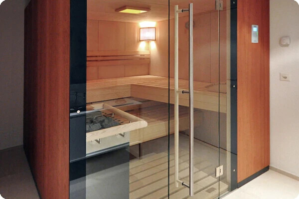 Glass sauna with wooden walls, glass front, wooden bench, and heater, warmly lit.