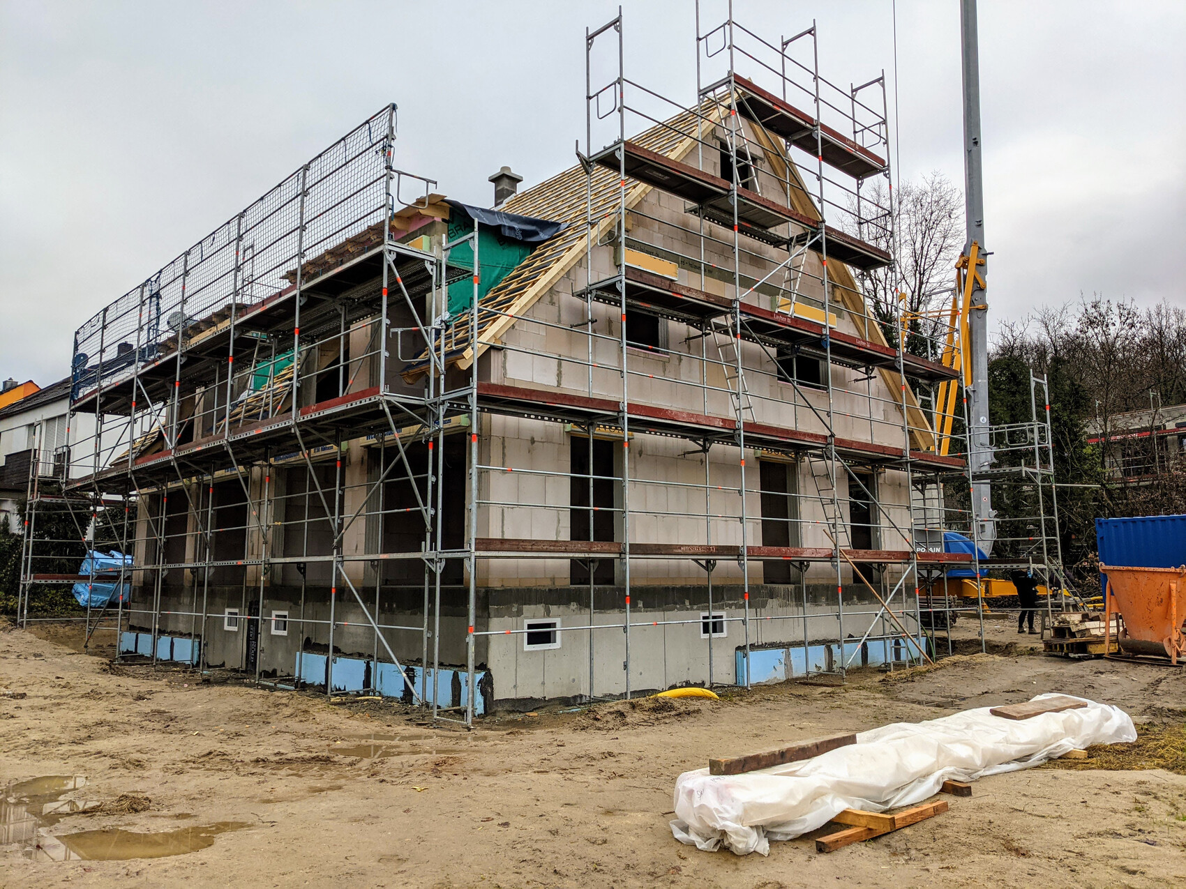 Mehrstöckiges Haus im Rohbau mit Gerüst und Baumaterialien auf der Baustelle.