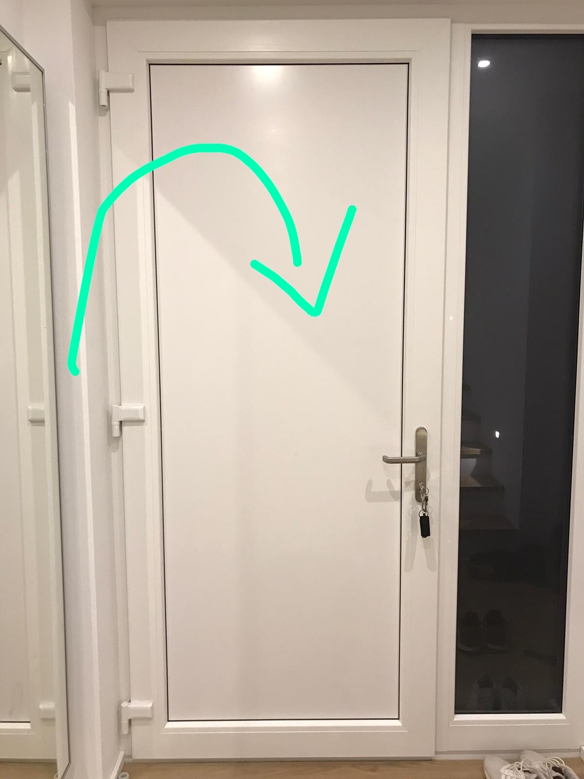 White door with green drawn arrow; handle on right with keychain; glass window on right shows stairs.