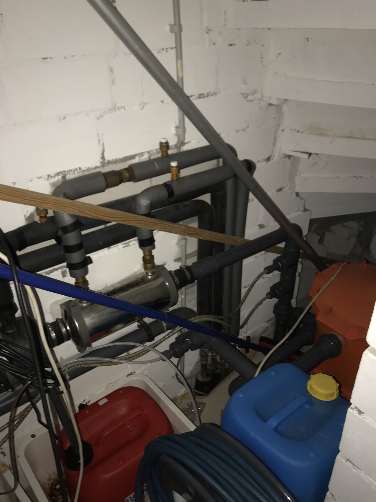 Basement utility room with pipes, valves, pump, cables and blue container.