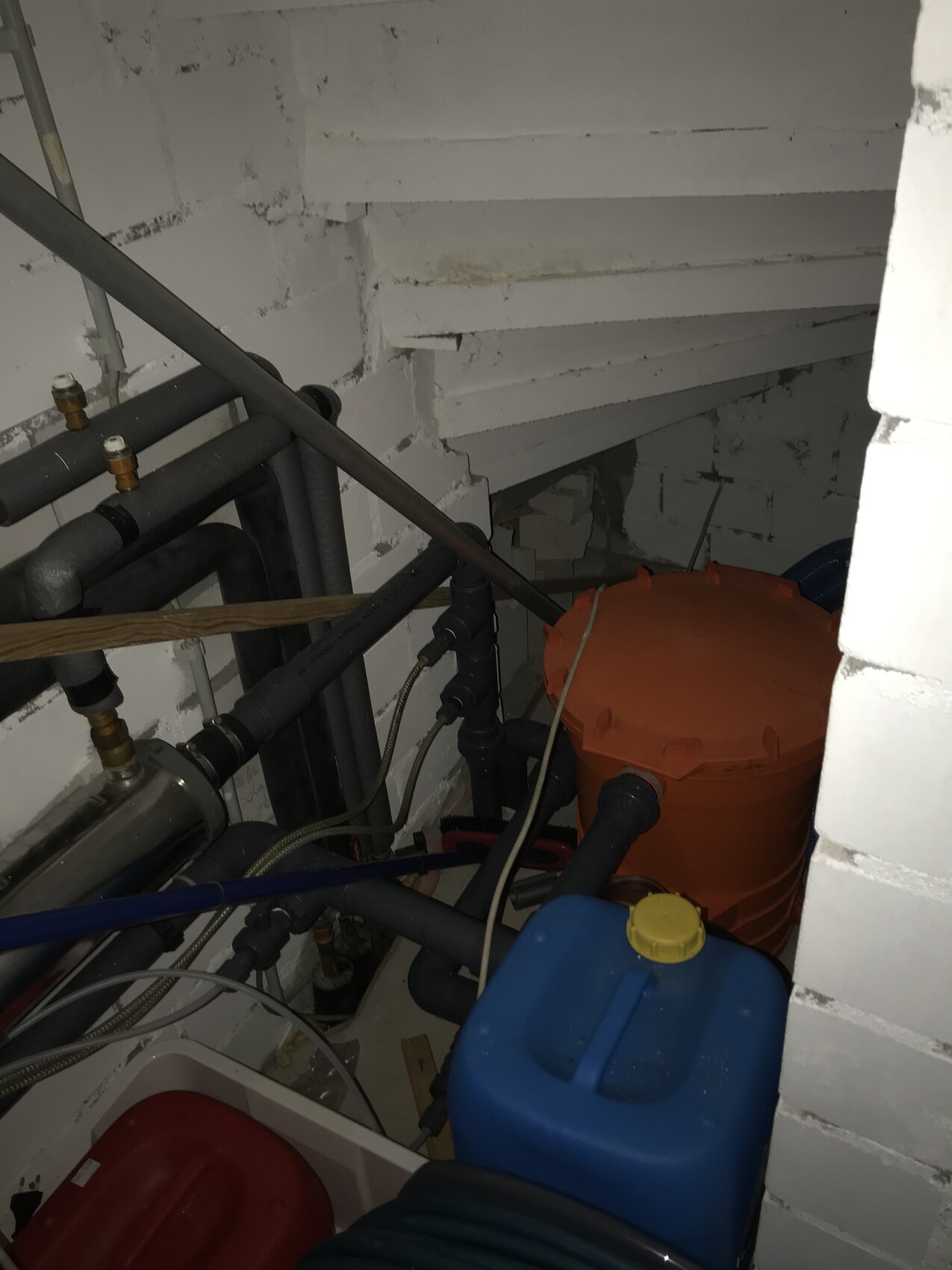 Basement room with piping, pump, orange cylinder tank and blue container.