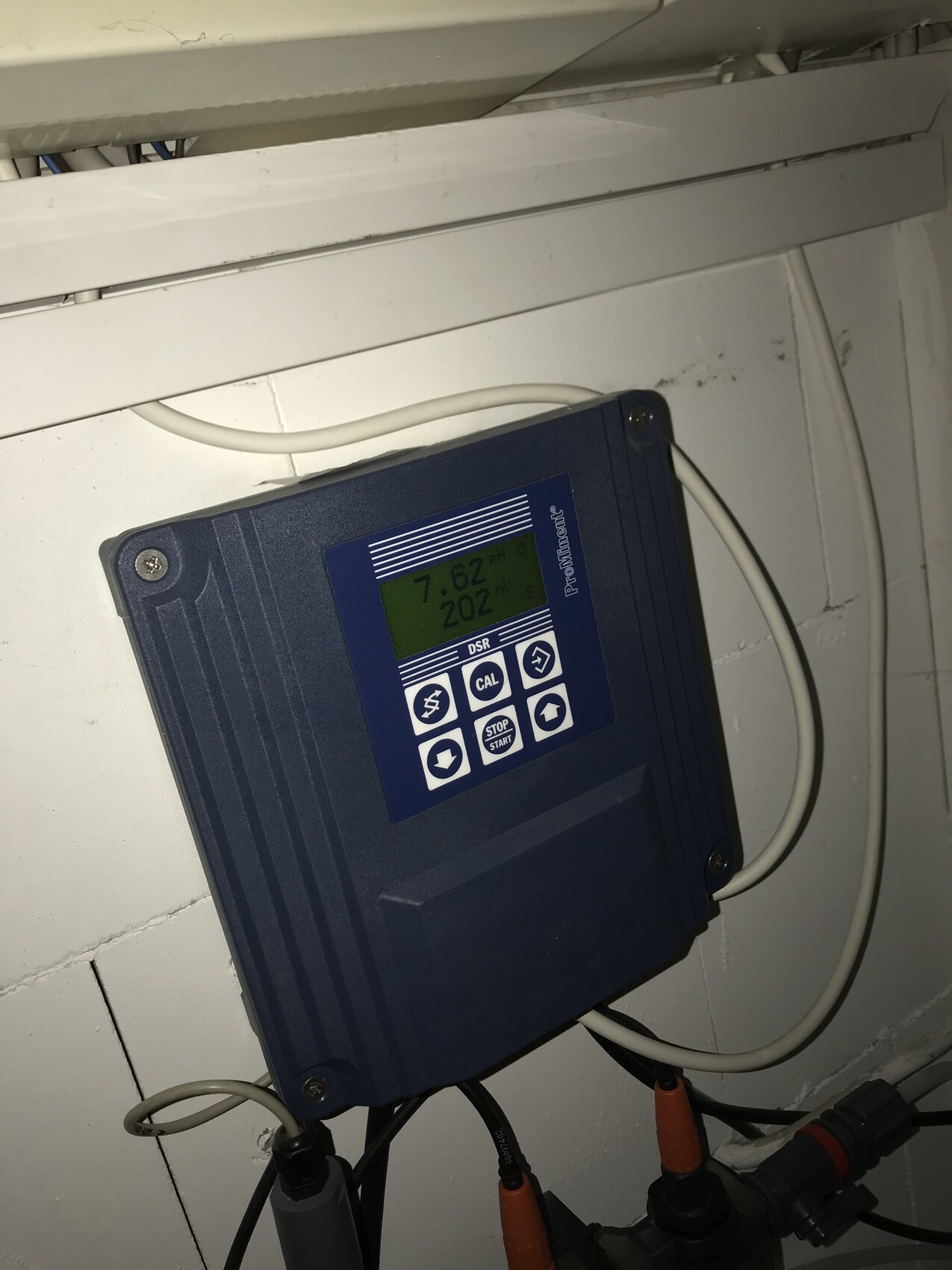 Blue electronic dosing device with display on the wall, cables connected.