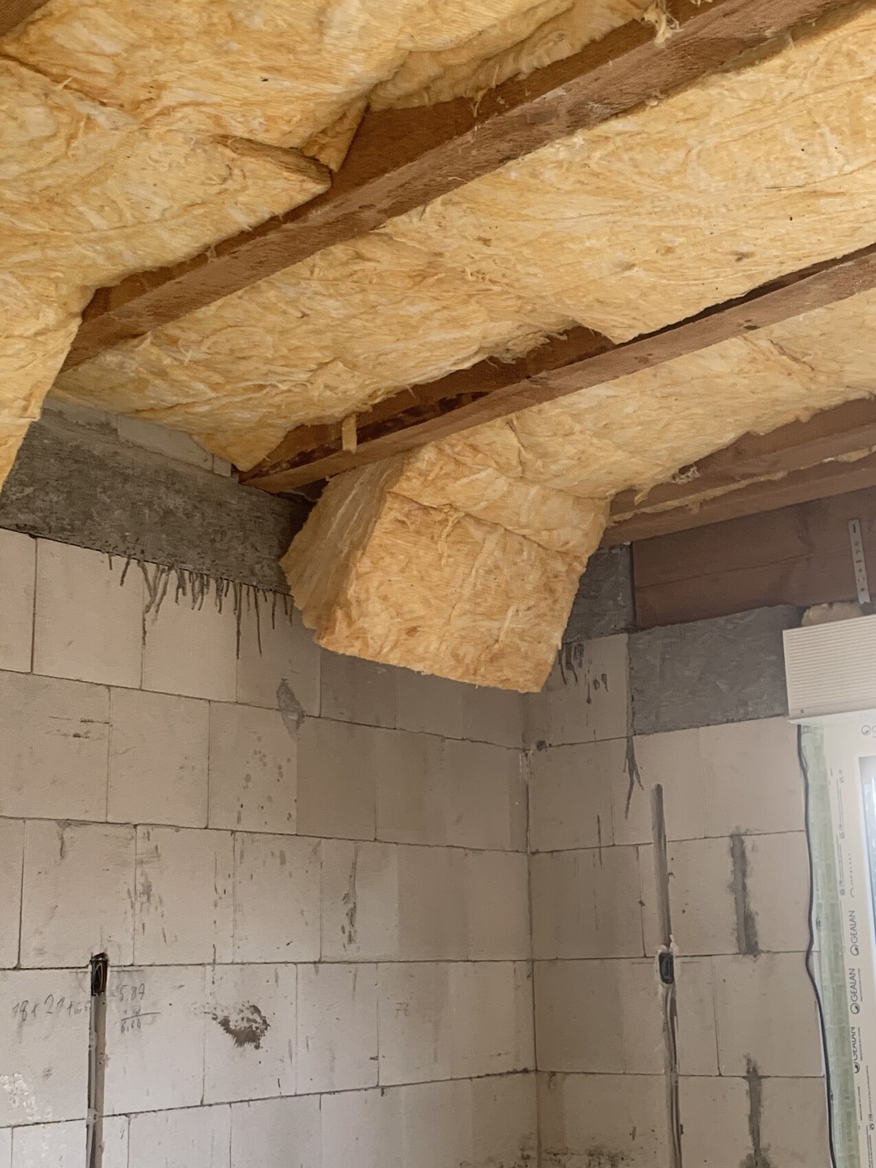 Interior of a construction site: Yellow mineral wool insulation panels between ceiling beams, white block walls.
