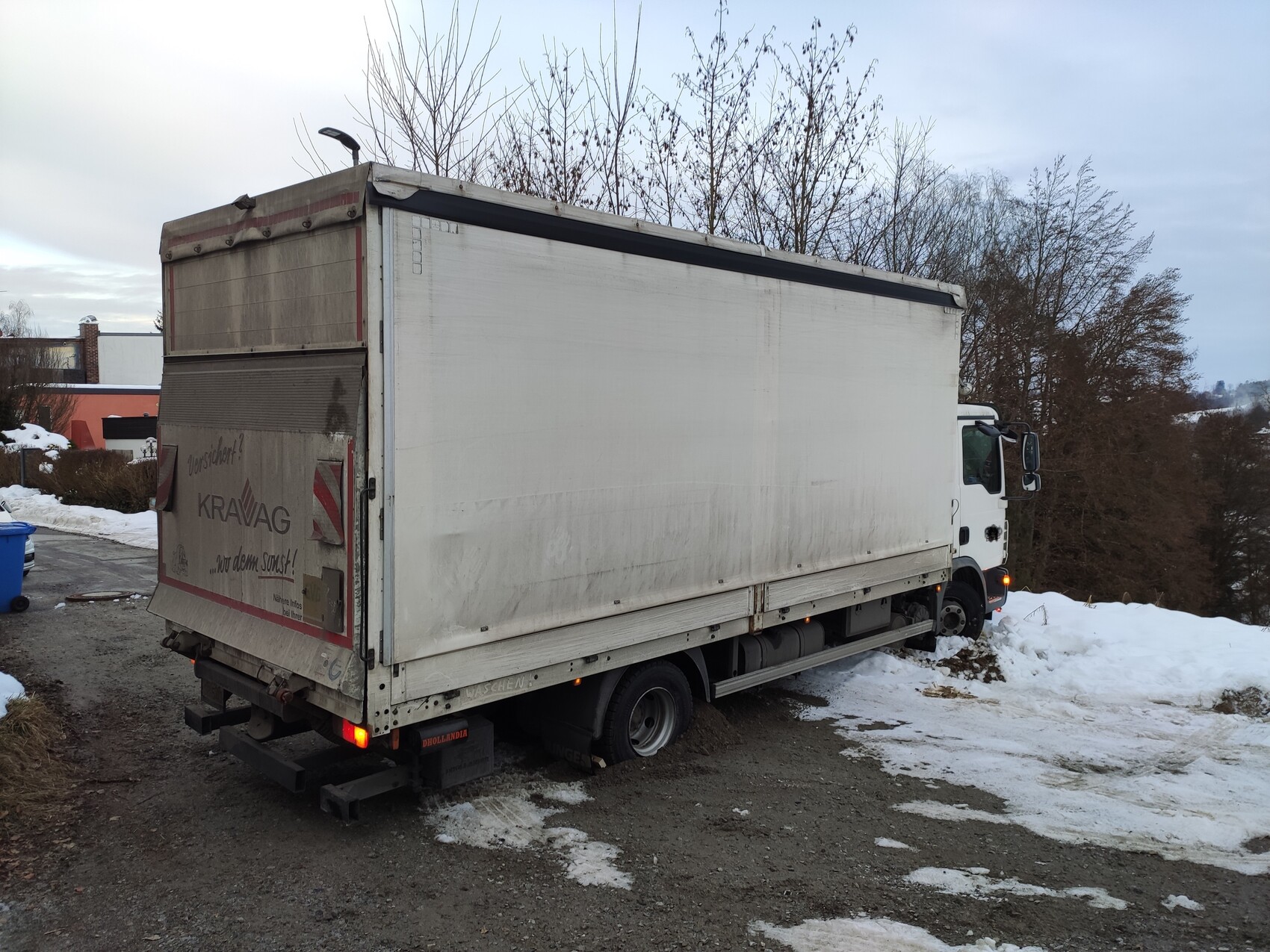 Large white truck with box body standing in snow; forest in the background.