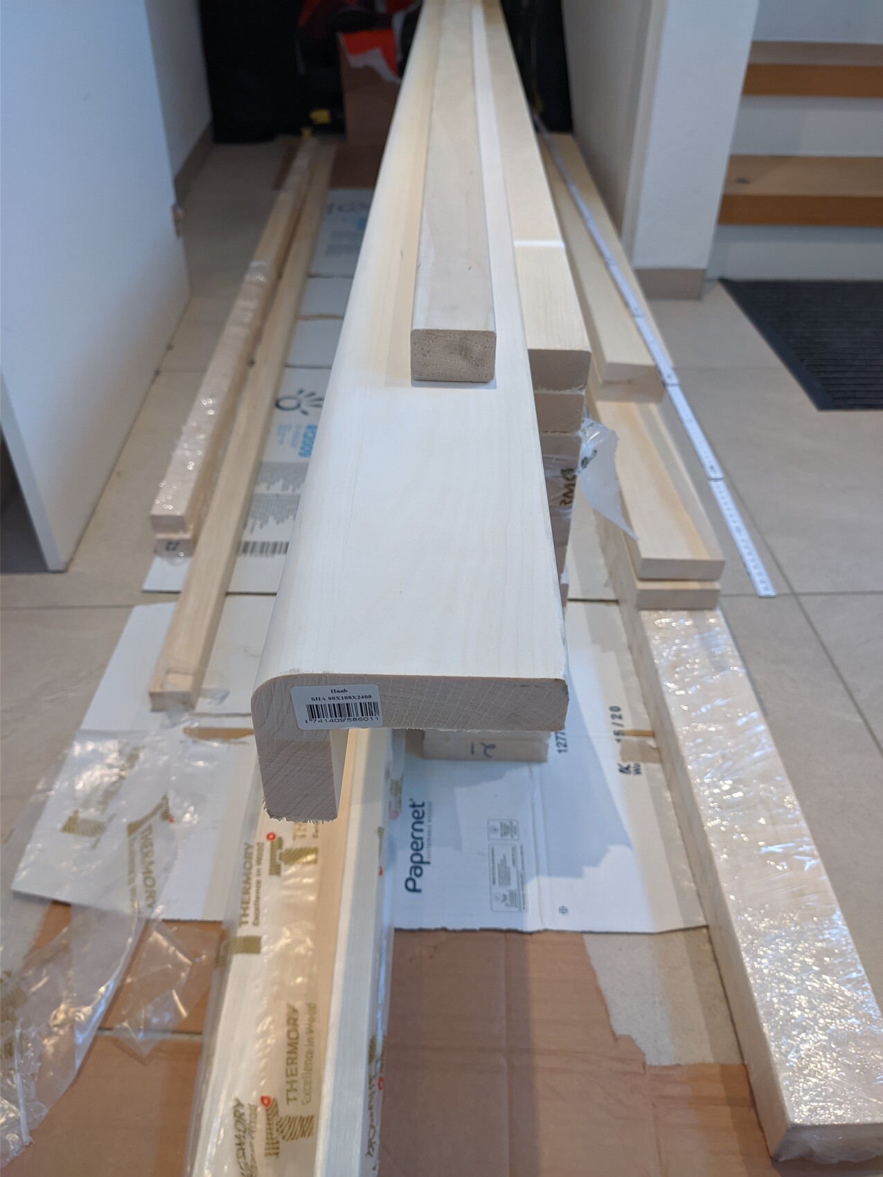 Long, light wooden beams lying on the floor of an interior; packaging material scattered around.