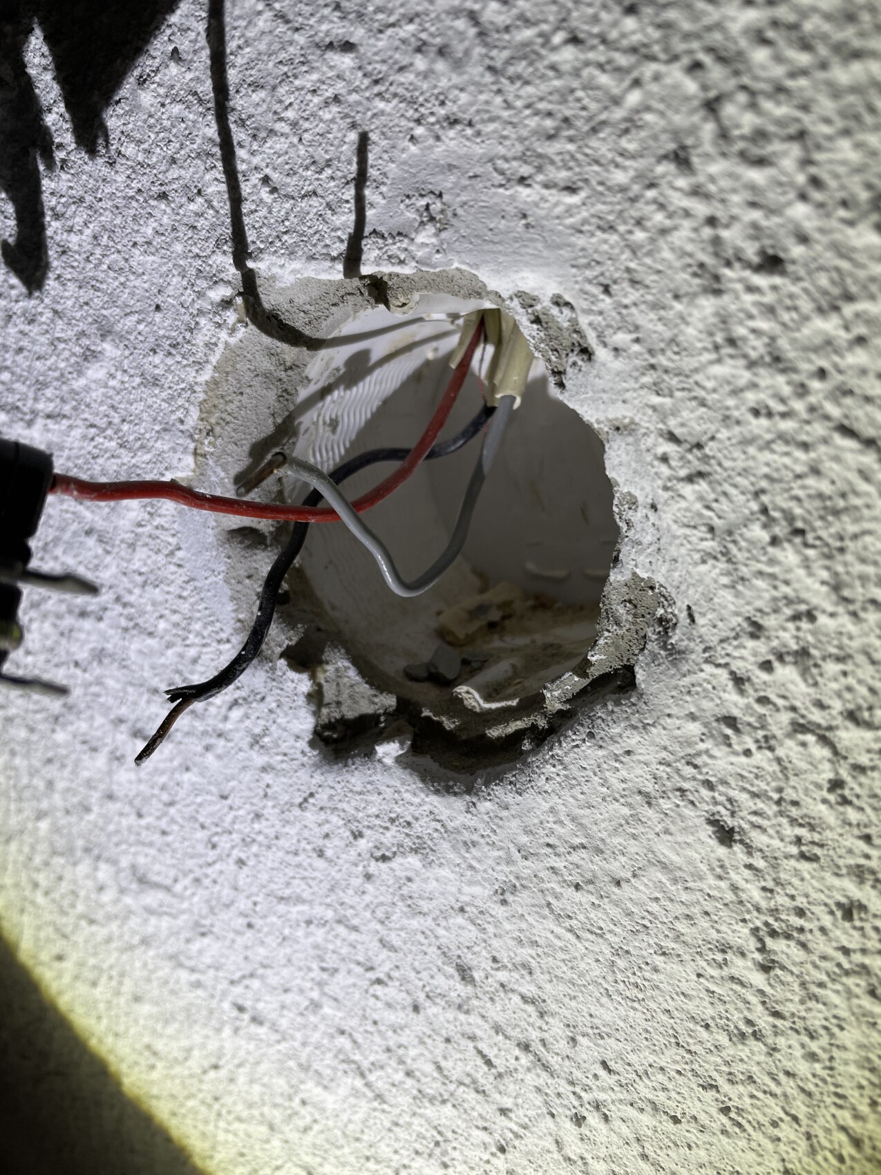 Exposed electrical cables in a wall opening; bundle of red, black and gray cables.