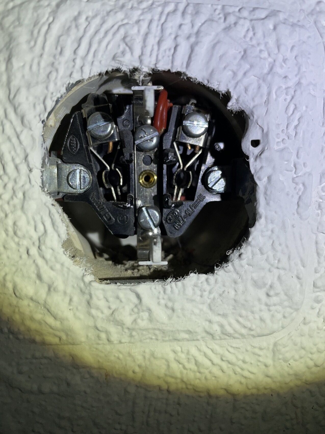 Close-up of the inside of a flush-mounted junction box with screw terminals and wire connections.
