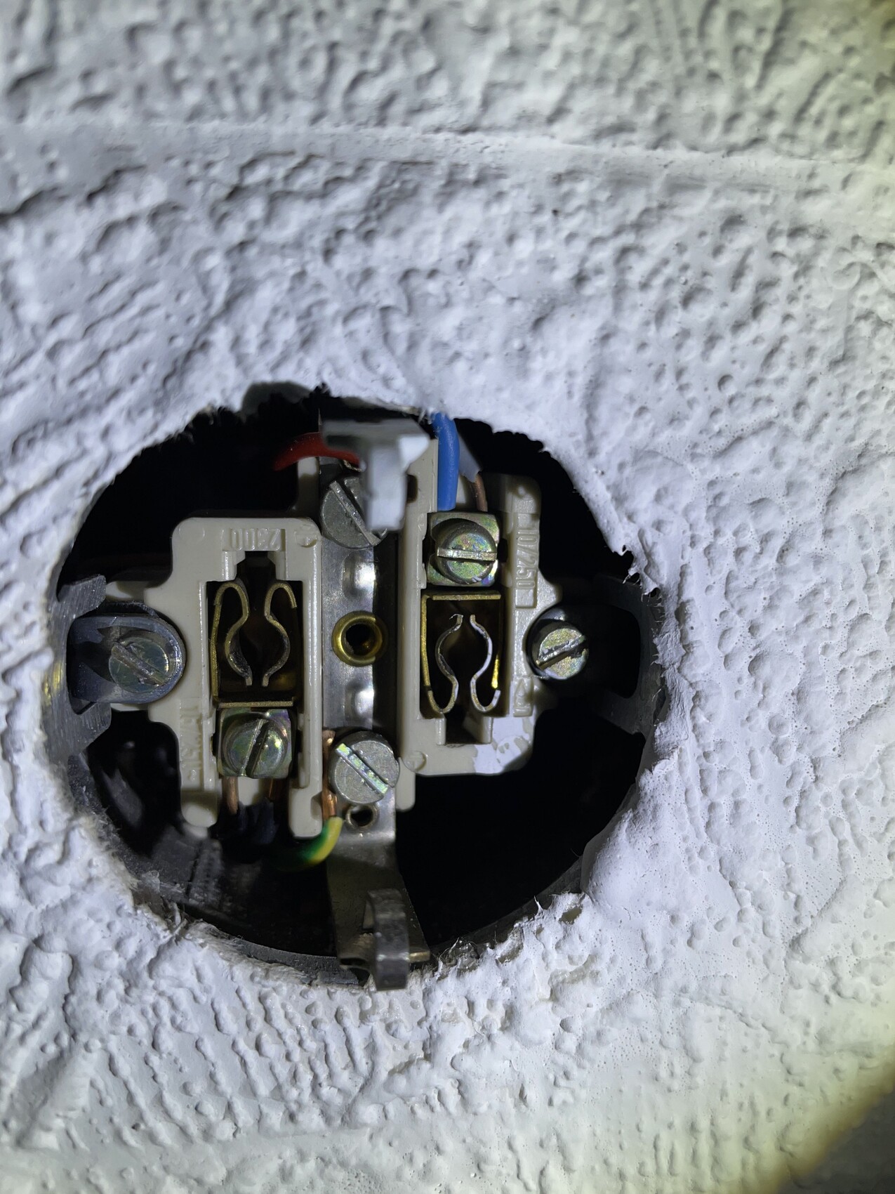 Close-up of an open flush-mounted box with wire terminals (blue, brown, green-yellow).