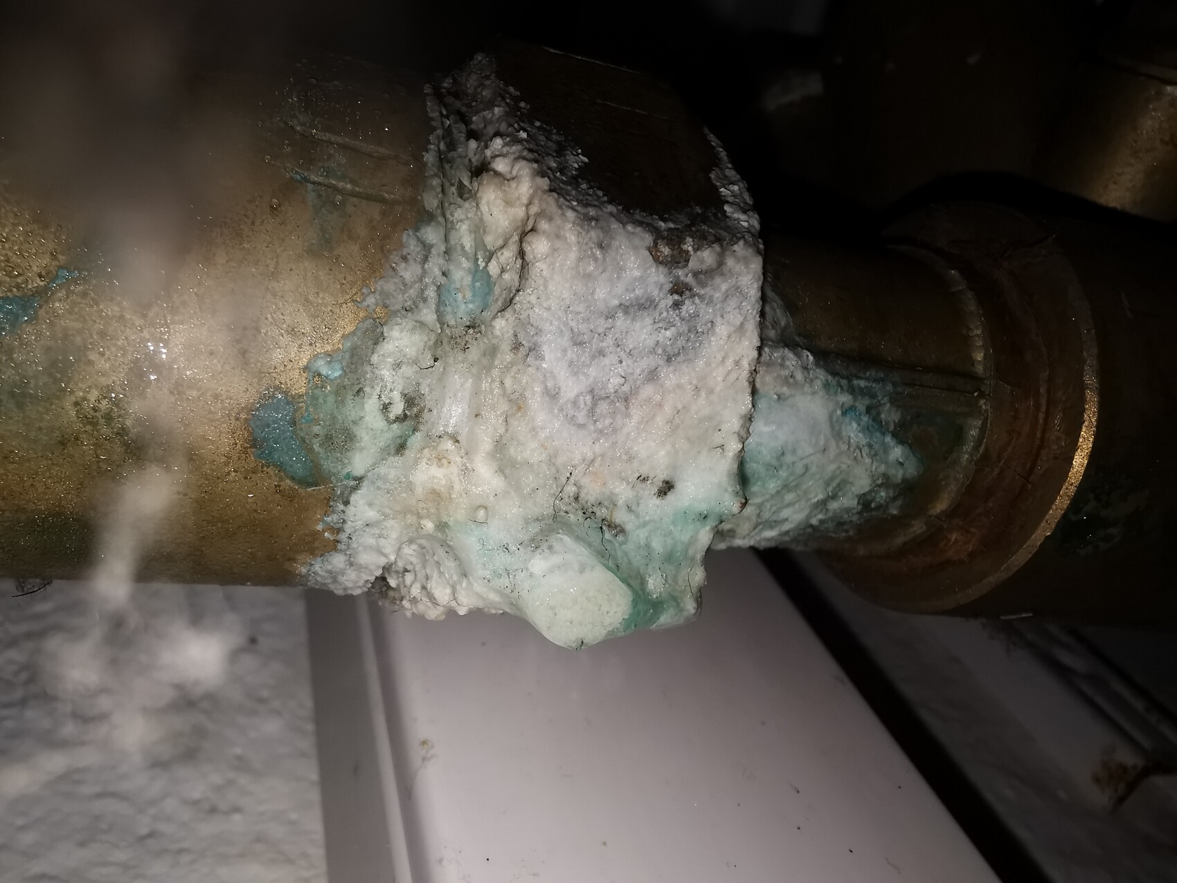 Copper pipe with white mineral deposits and greenish-blue corrosion at the pipe joint