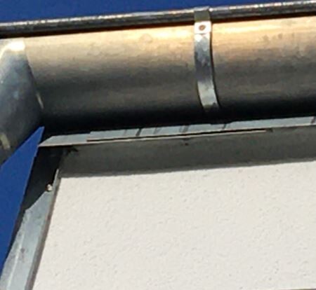 Exterior pipe at the edge of a building’s roof, mounted sideways on a white wall