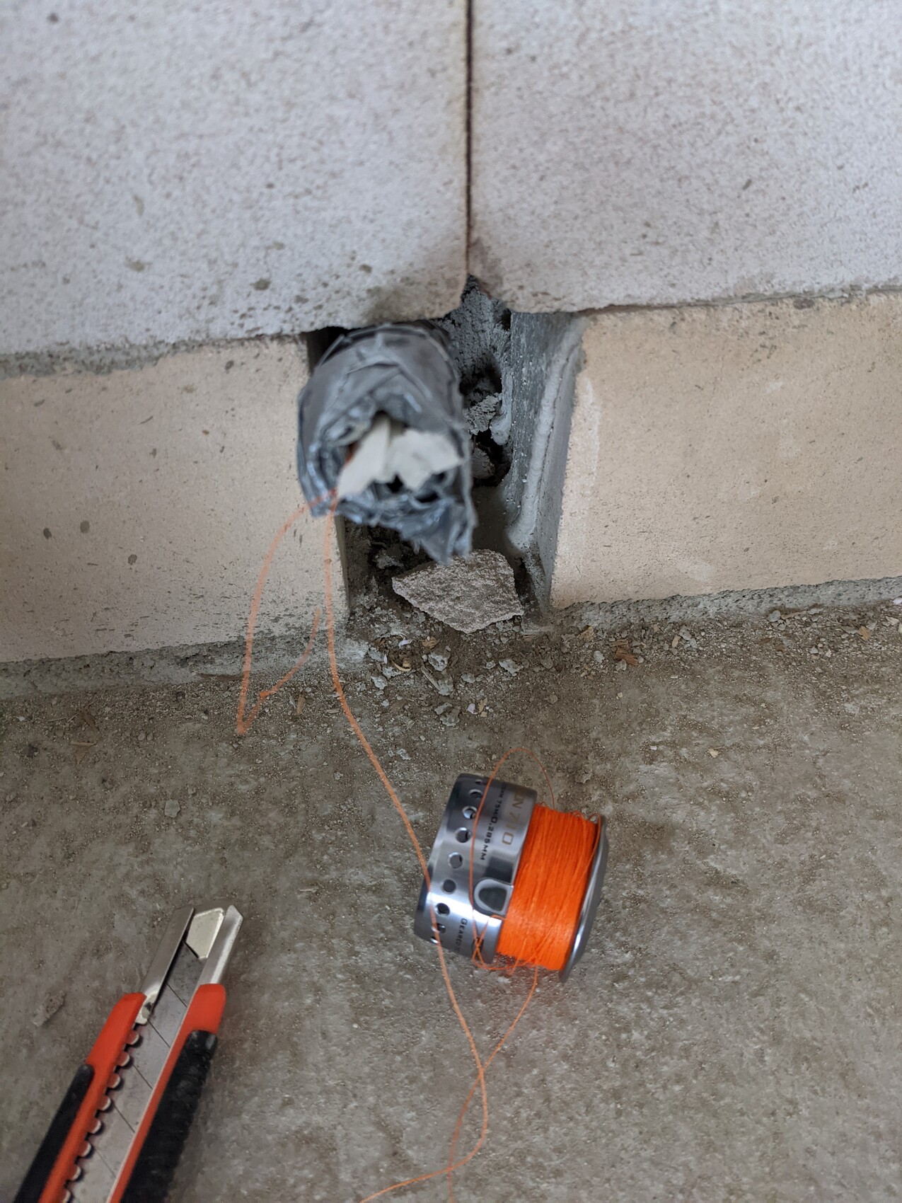 Open wall hole in concrete wall, loose cable, orange cord on spool, cutter next to it.
