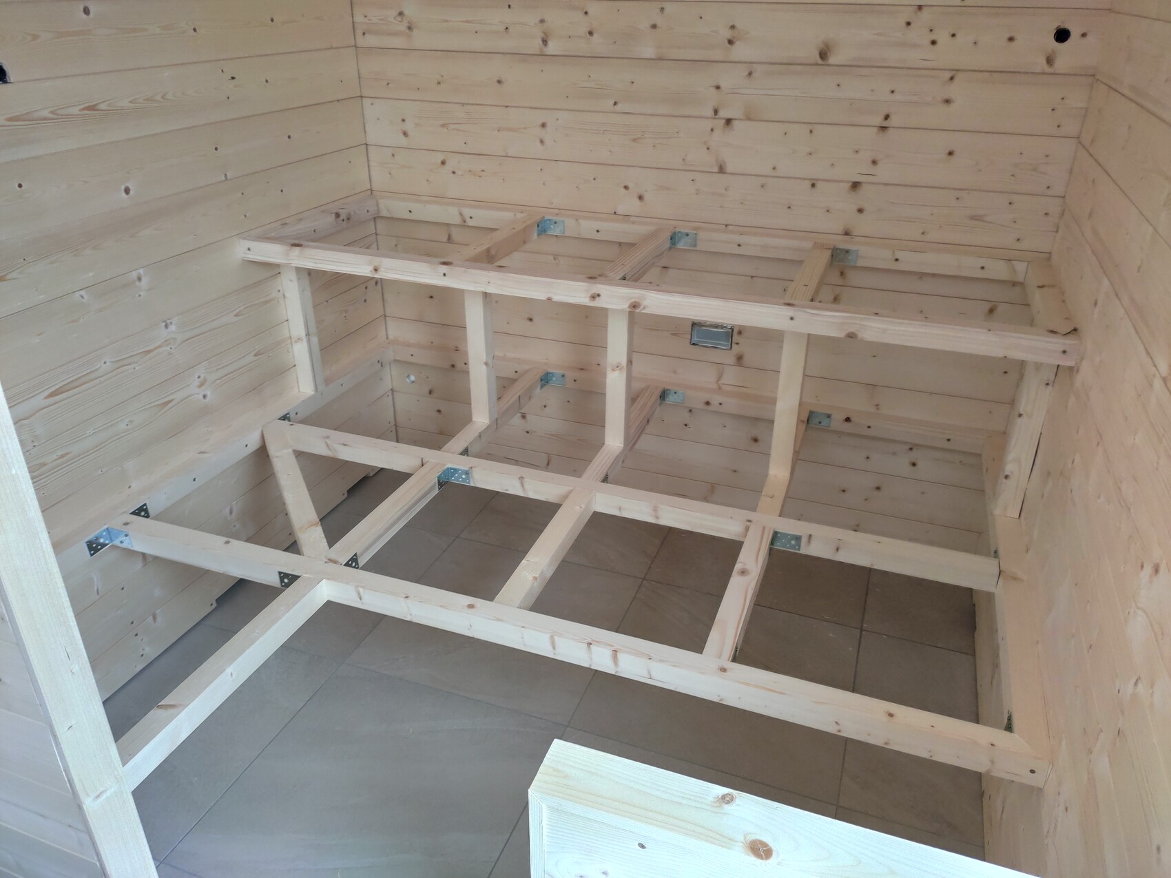 Unfinished wooden bed base made of beams with metal brackets inside the room.