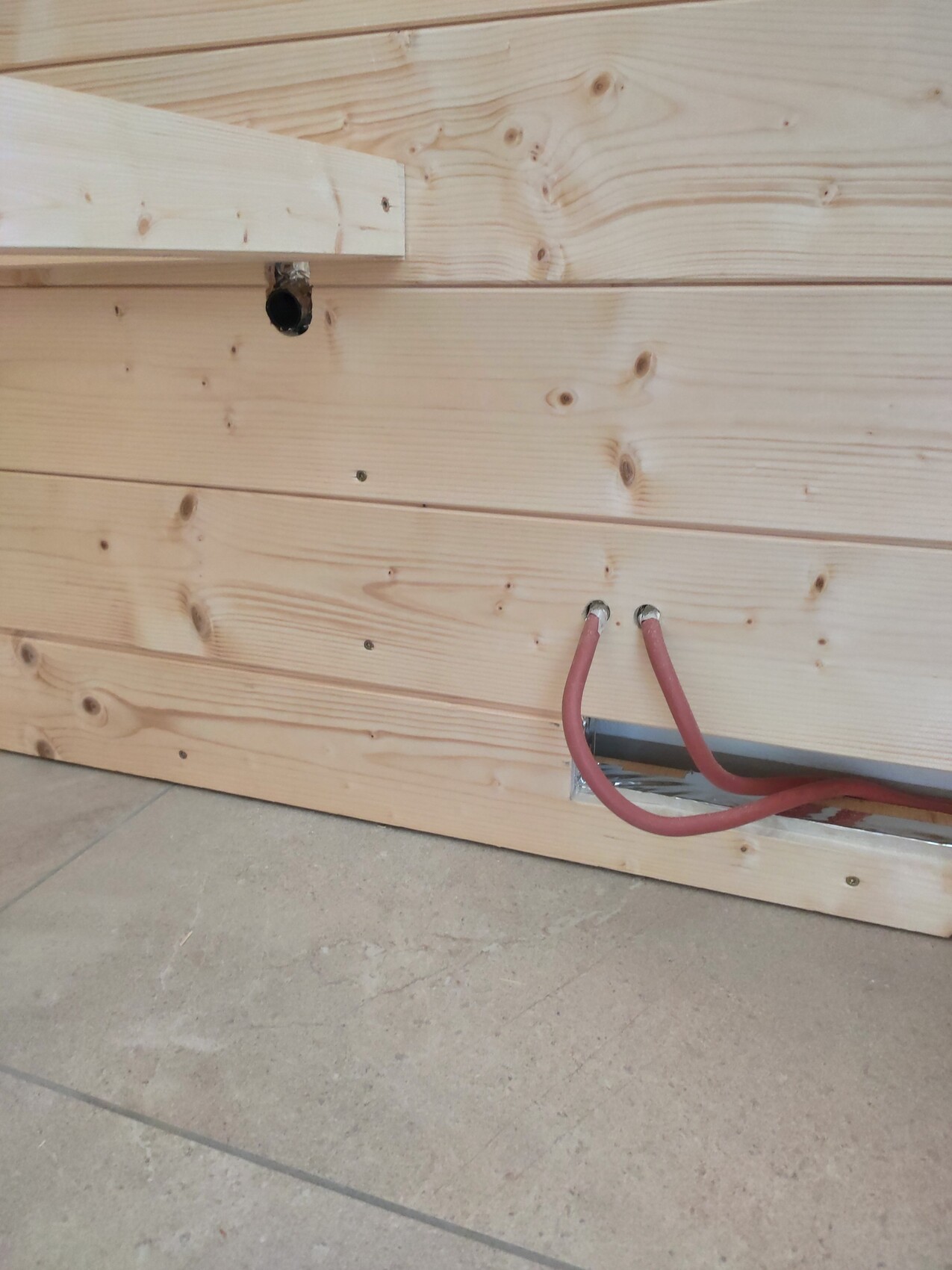 Two red cables protruding from an opening in the lower wooden panel of the wall; concrete floor below.