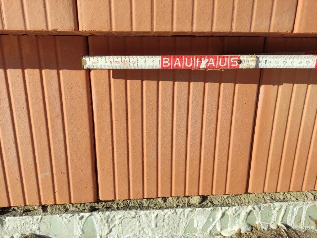 Tape measure with BAUHAUS print lying horizontally against red brick wall.