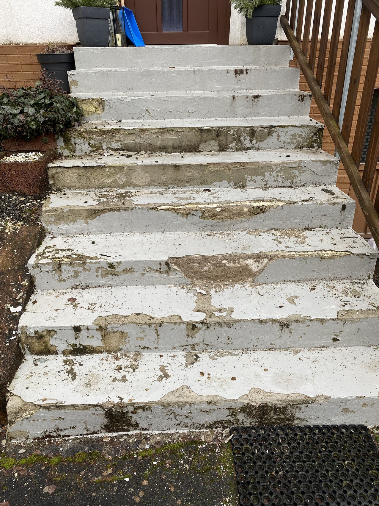 Worn grey concrete steps lead to the front door; moss, cracks, and dirt are visible