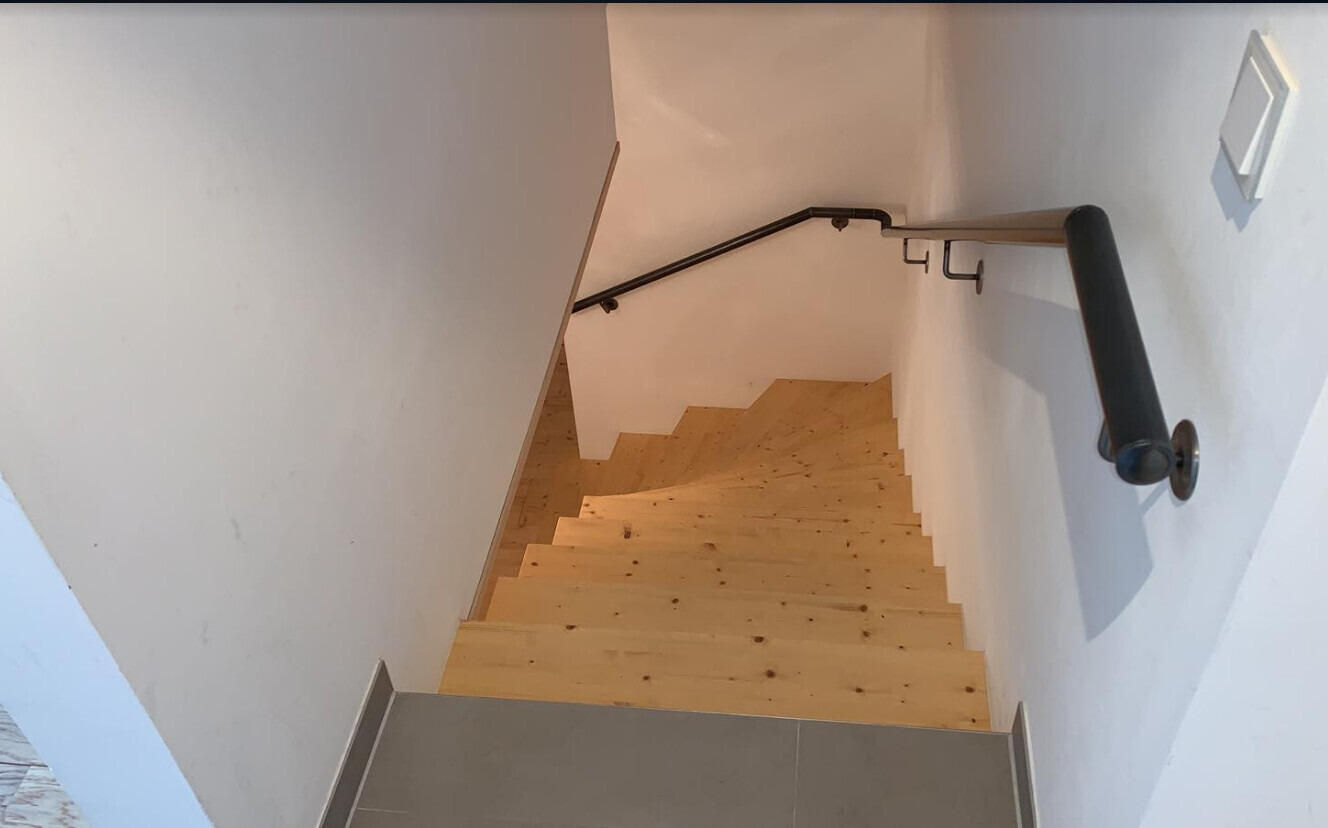 Light wooden stair steps with black railings on the left and right, view looking down.