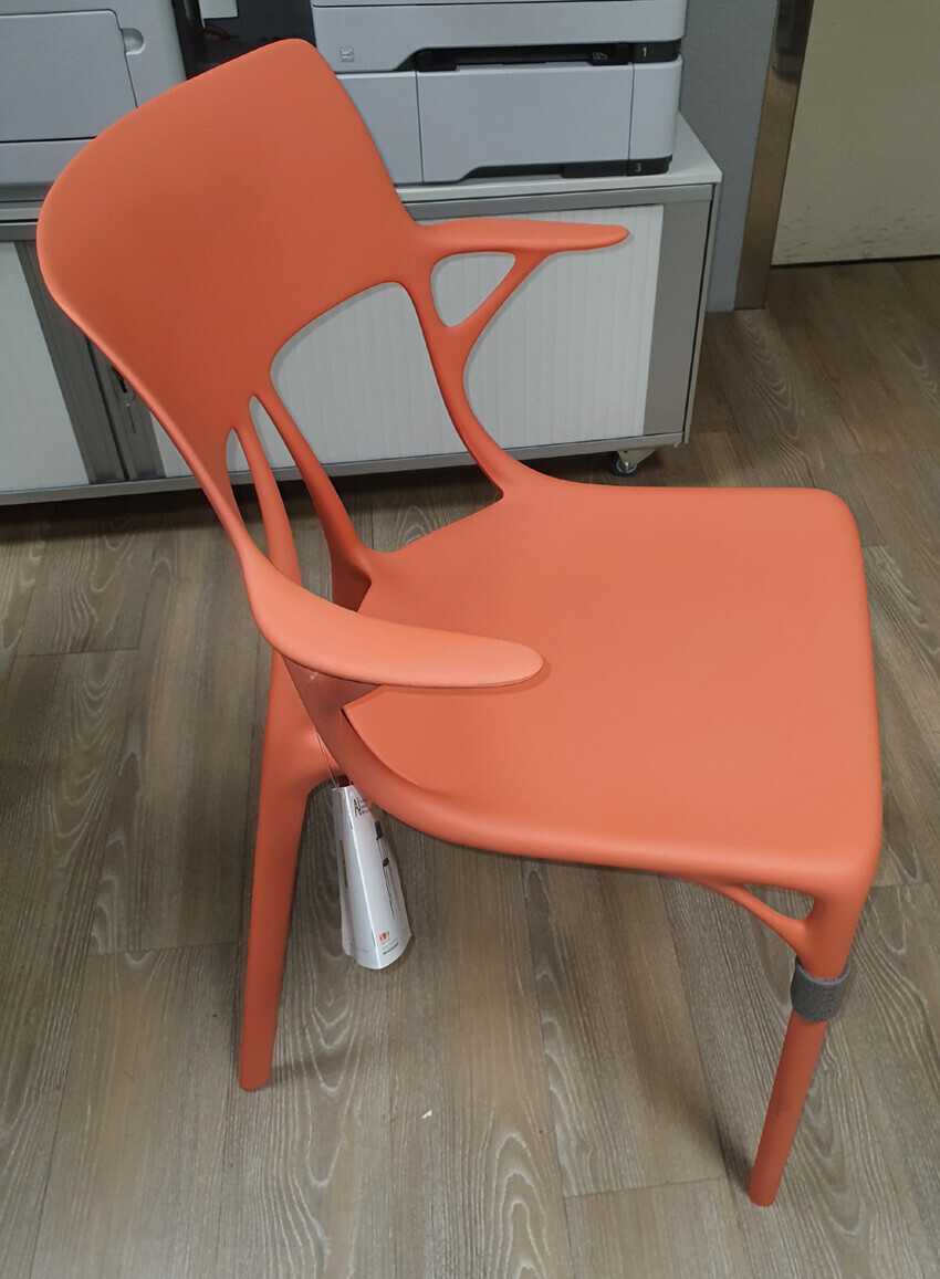 Orange modern plastic chair with cutouts in the back in front of a copier in an office.