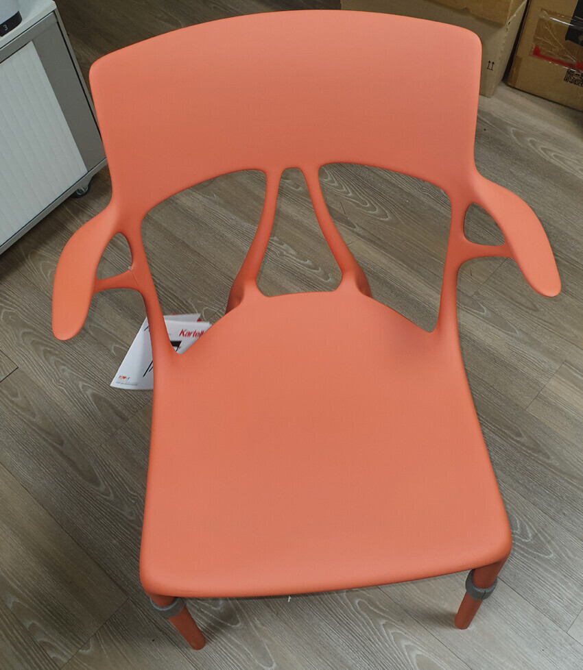 Orange plastic chair with armrest cutouts on a wooden floor.