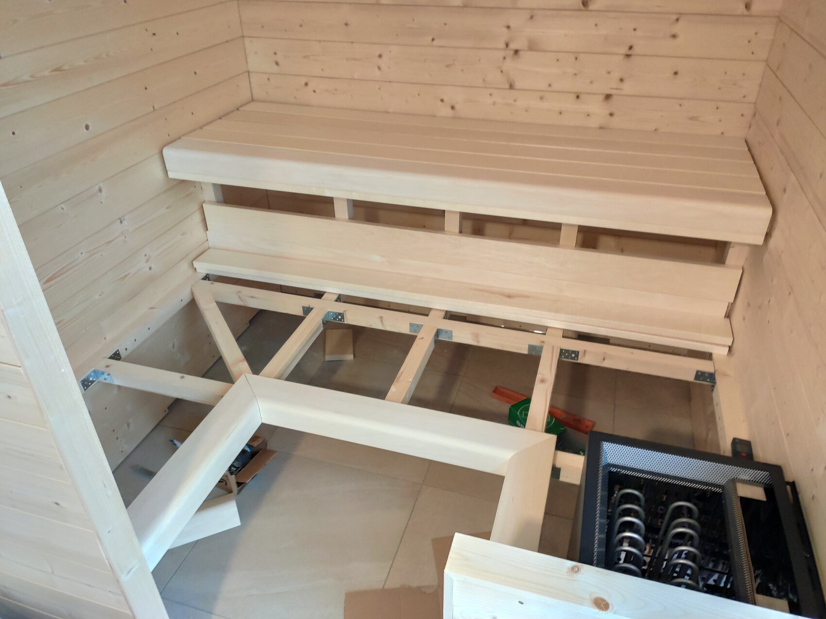 Interior of a wooden sauna with two staggered benches and a heater on the floor.