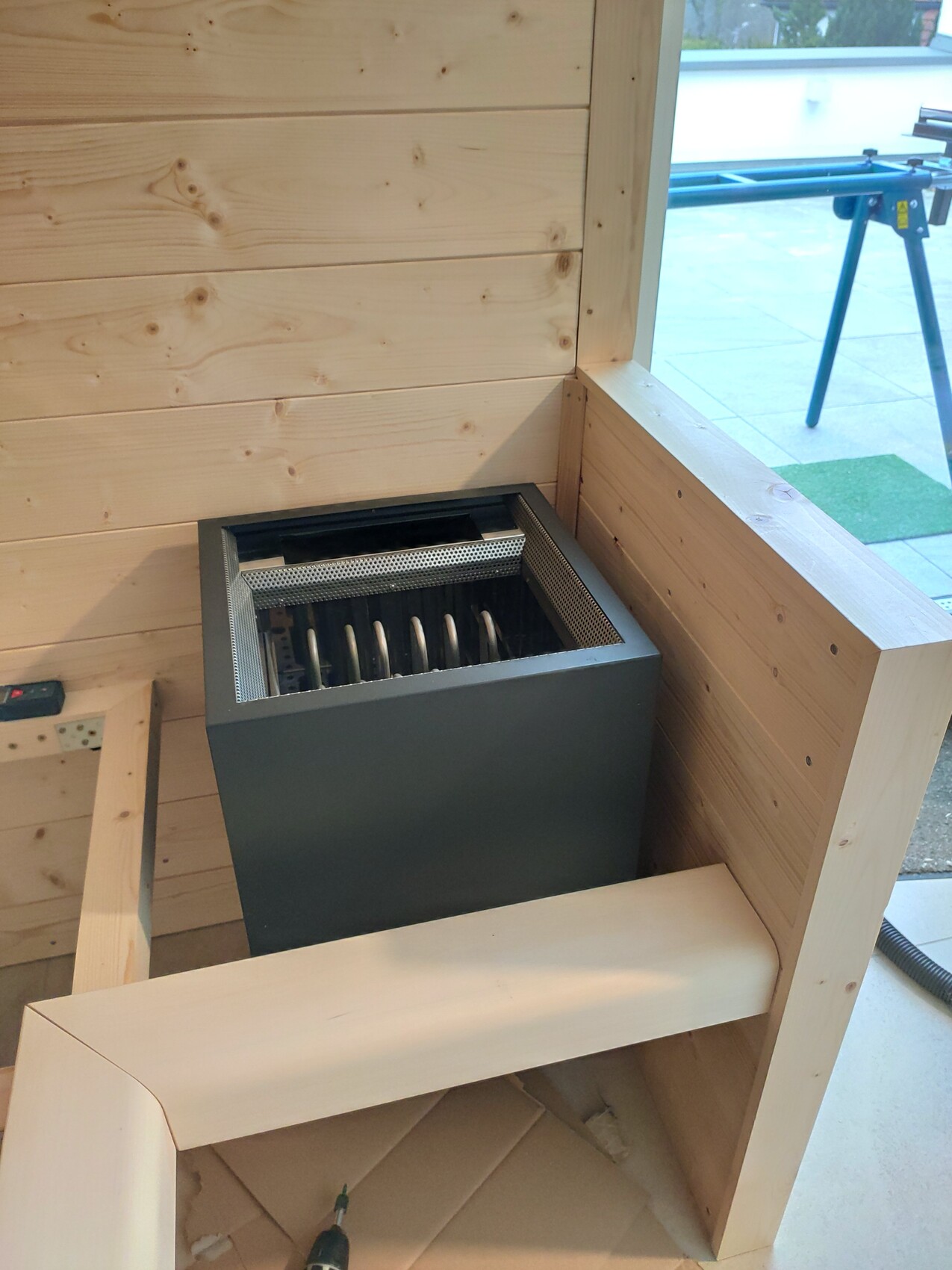 Small heater stove in a wooden room, metal housing and grill visible.