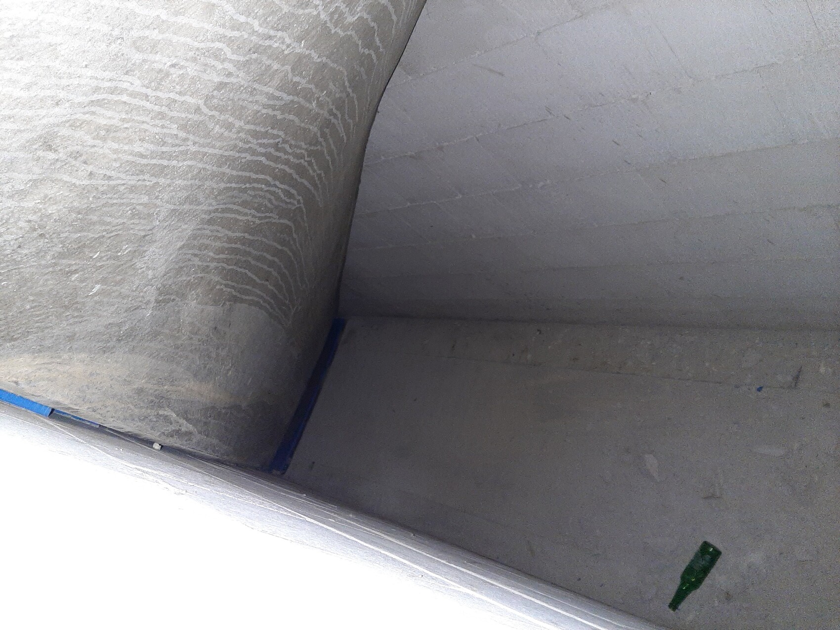 Concrete room with curved wall, blue tape on the edge, dusty; green bottle on the floor.