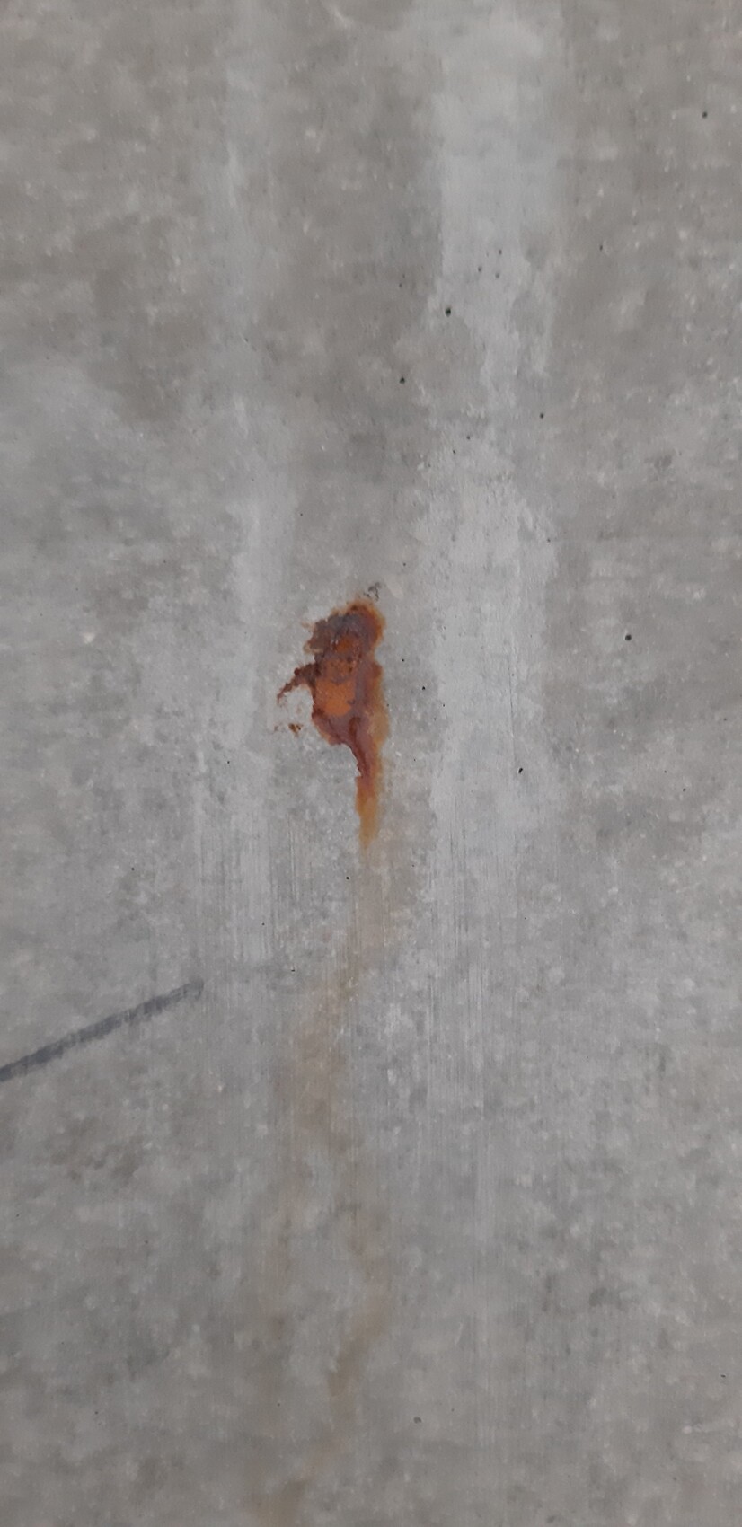 Kleiner rostorangefarbener Fleck auf grauem Betonboden mit Tropfen.