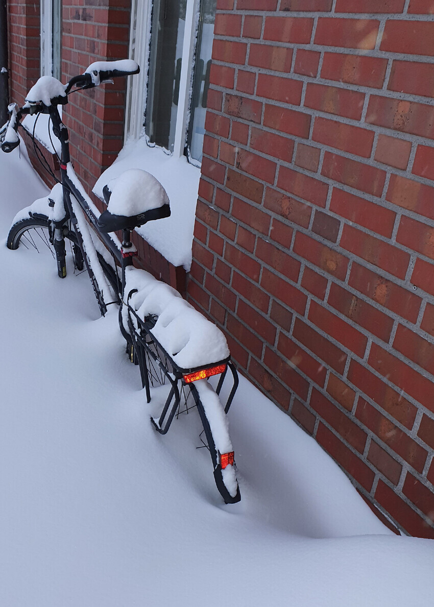 Bicycle in front of red brick wall, heavily covered with snow, saddle and handlebars covered