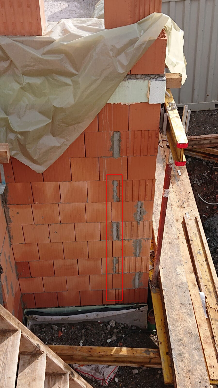 Construction site brick wall made of red bricks, visible mortar joints, upper foil covering the wall.