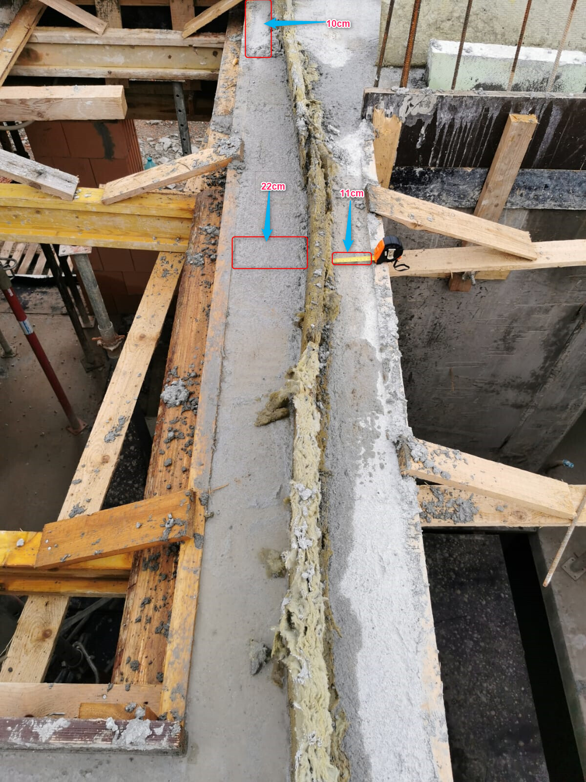 Construction site: concrete beam with joint, sealing compound, wooden framework, and measurement marks.