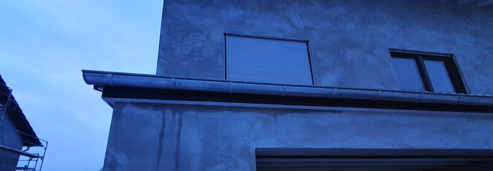 Gray building facade with closed roller shutter window and gutter