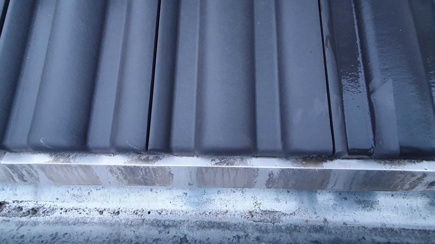 Close-up of dark metal roof flashing with vertical ribs and dirty edges