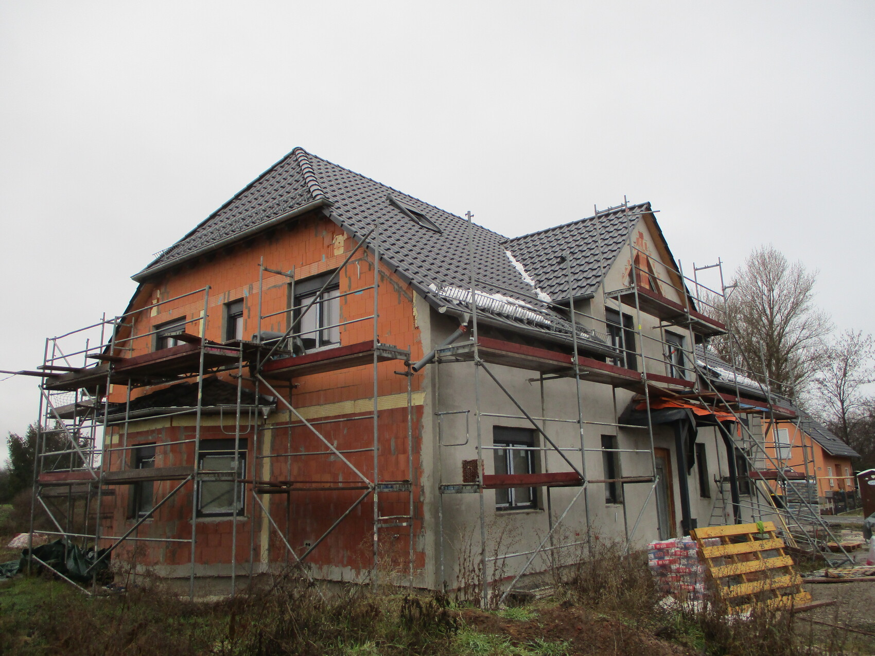 Mehrfamilienhaus im Rohbau mit Gerüsten, roten Backsteinen und Ziegeldach