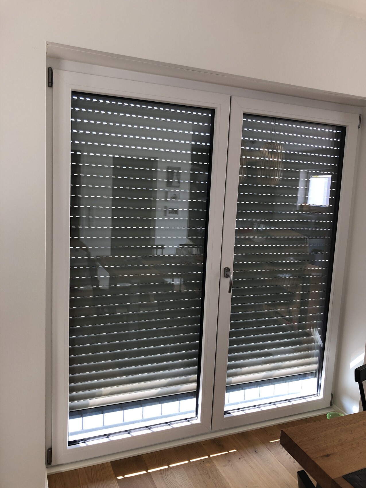 White double door with horizontal roller shutters, view into bright interior, wooden floor.