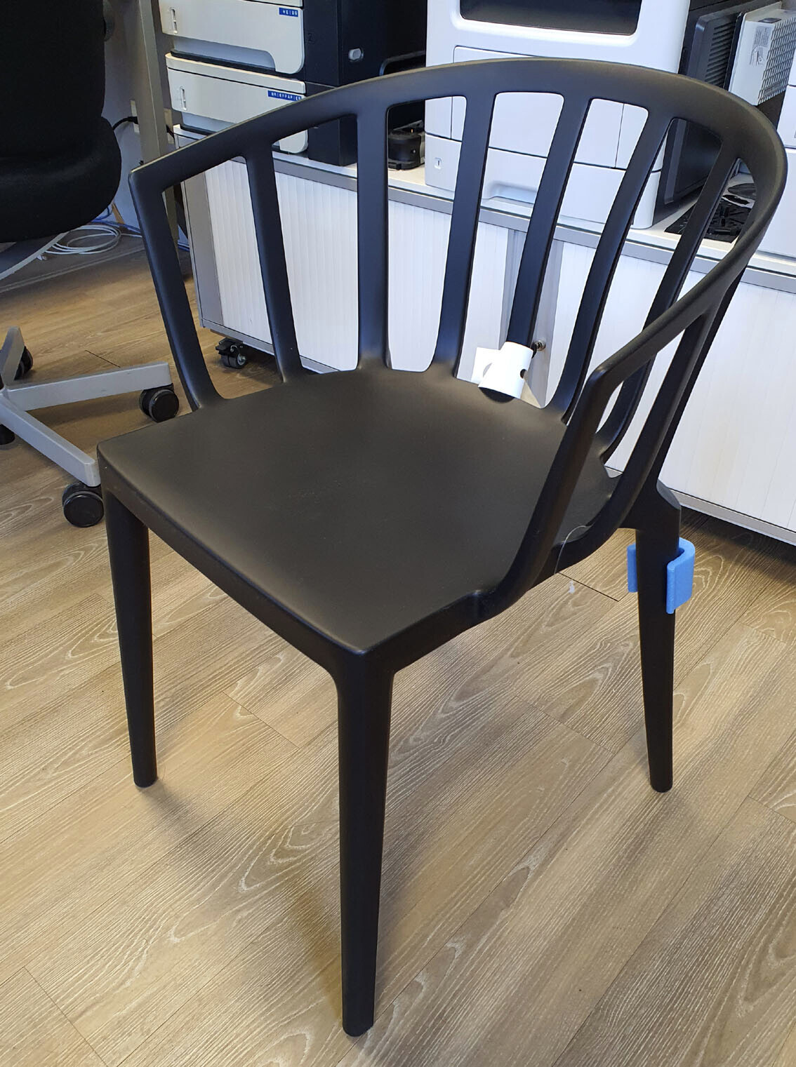 Black plastic chair with vertical backrest in an office setting in front of equipment.