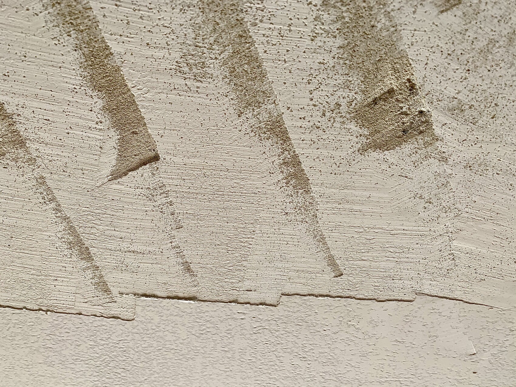 Close-up of a plastered wall with rough sand texture and diagonal lines.