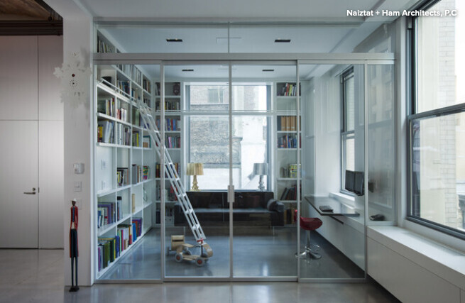 Open living room with glass partition, bookshelves on the left, rolling ladder, and sofa.