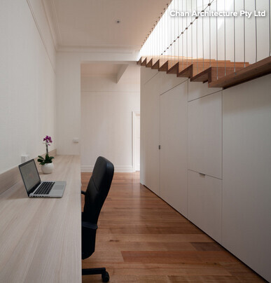 Modern workspace with desk, laptop, white built-in cabinets, and wooden staircase.