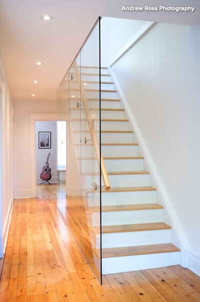Bright interior: wooden staircase with glass railing, white walls, guitar in the background.