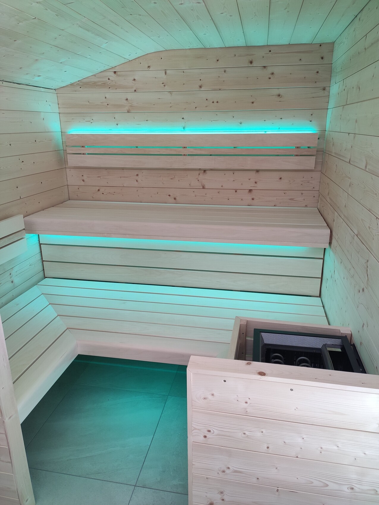 Wood sauna with two benches, turquoise lighting, and heater in the corner.