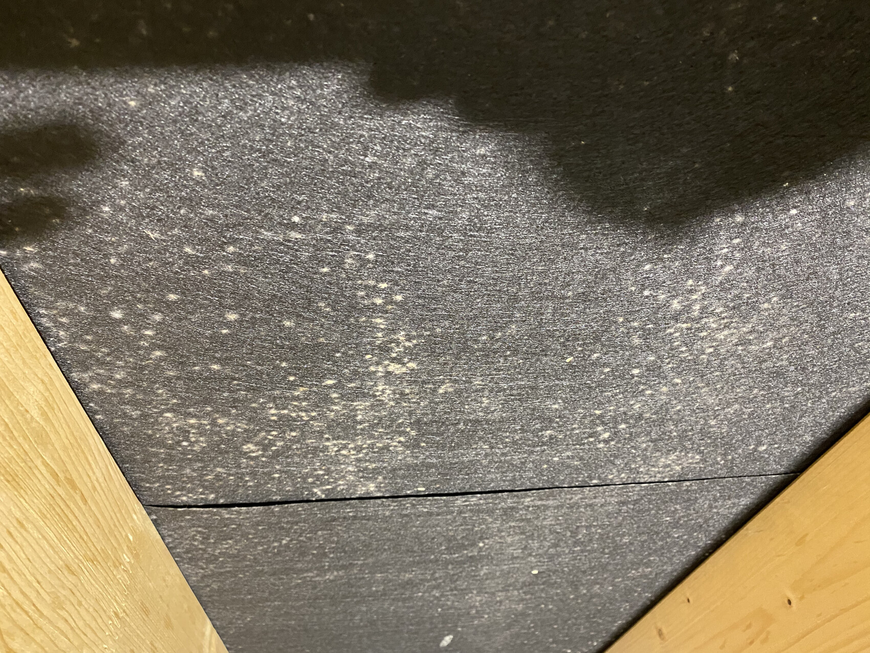 Dark, textured surface with many white dust particles, framed by wooden structure.