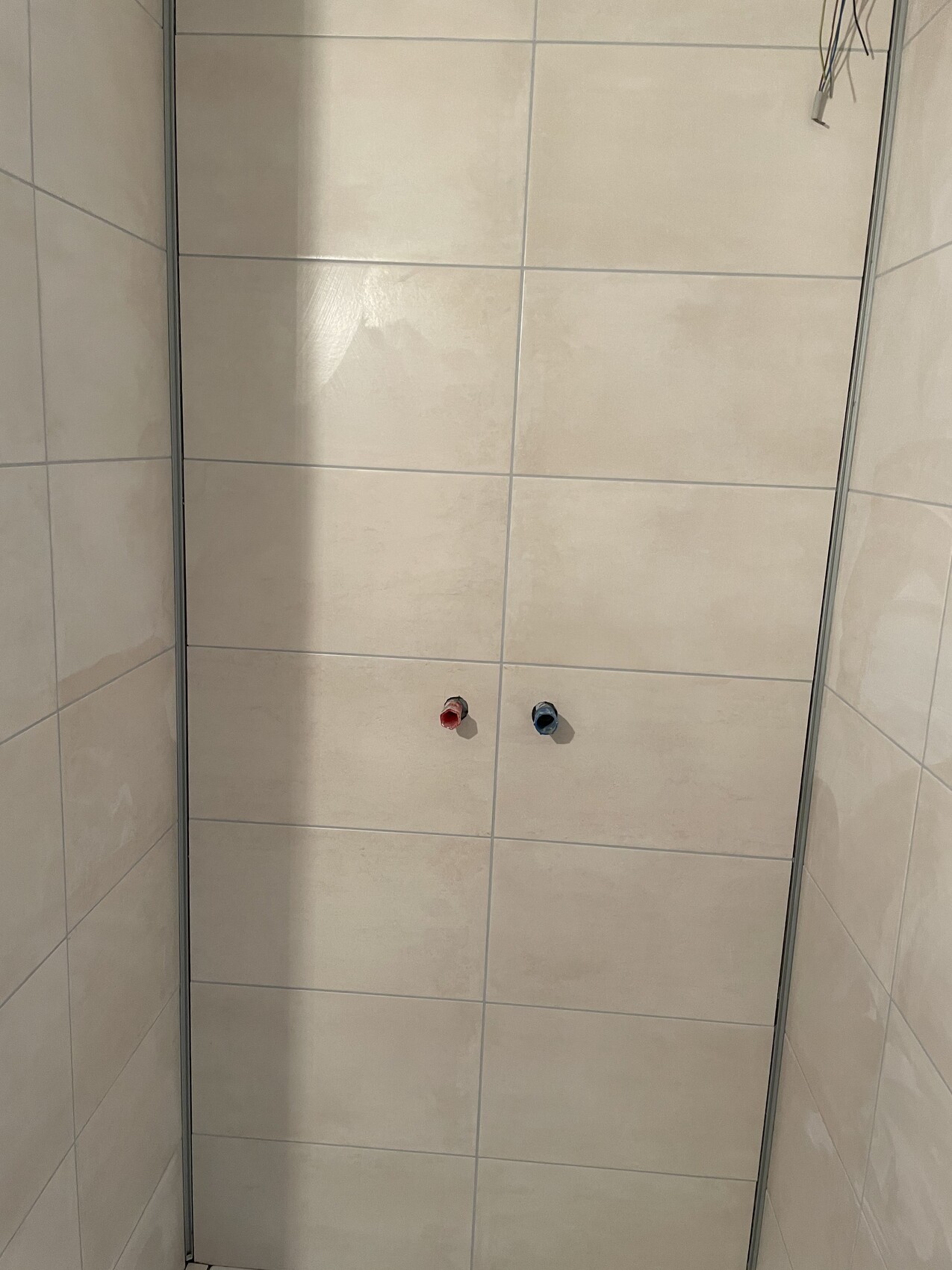 Shower enclosure with light wall tiles, two water connections (red/blue) on the wall.