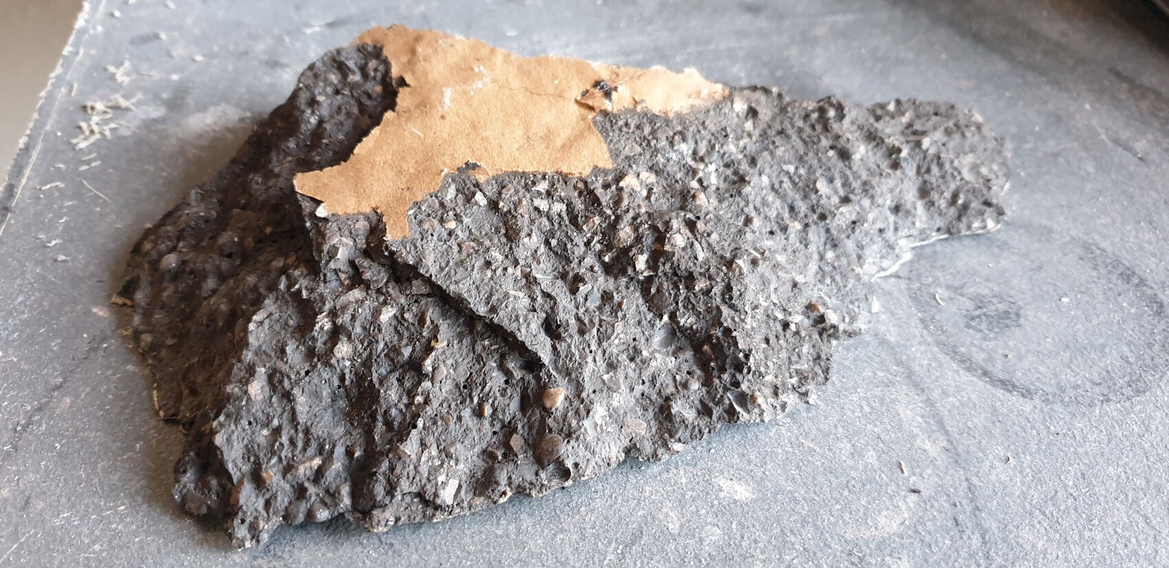 Dark, porous stone chunk with brown paper residue on gray background