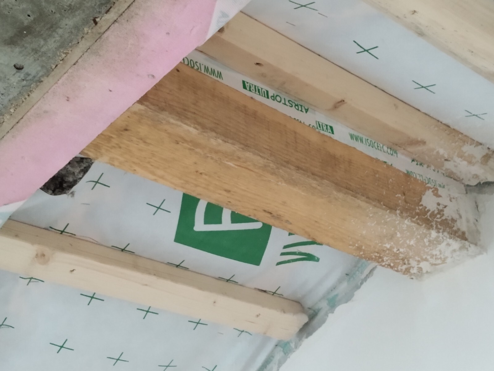 Innenbaustelle: Holzbalken, rosa Dämmstoff, Folie mit grünem Muster und Mörtelreste.