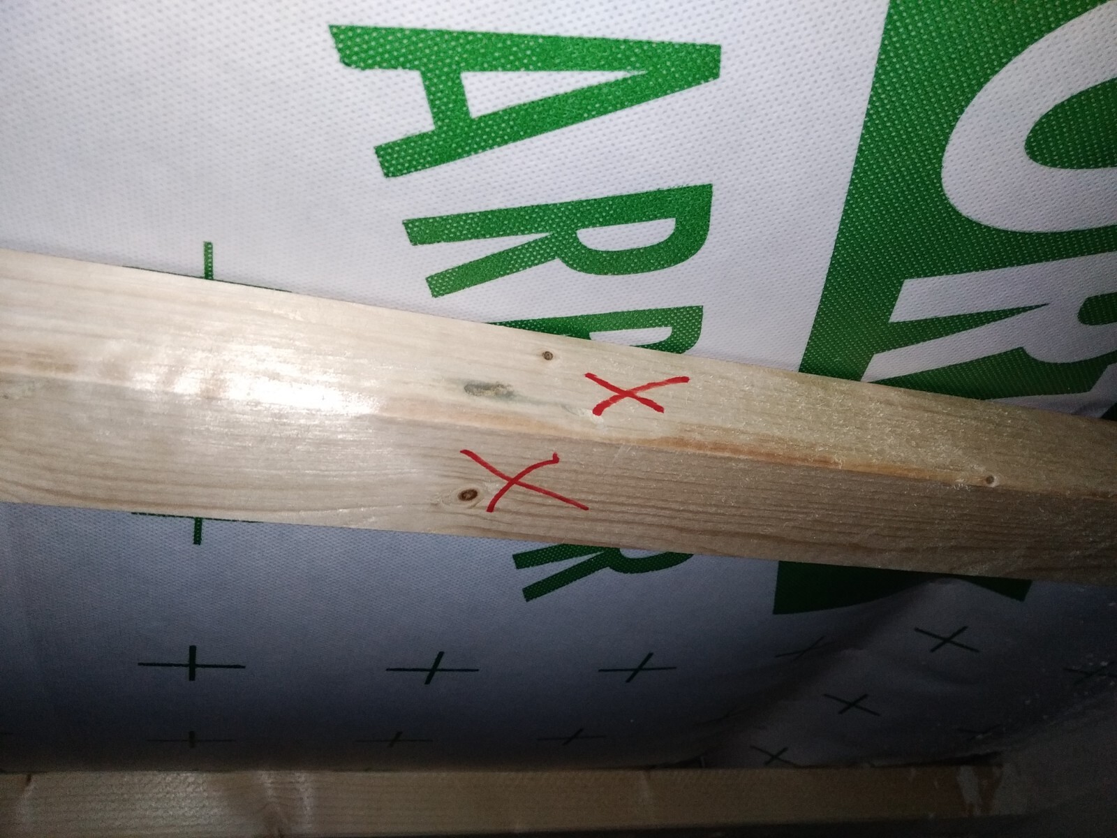 Holzlatte mit zwei roten X-Markierungen, Hintergrund: Baufolie