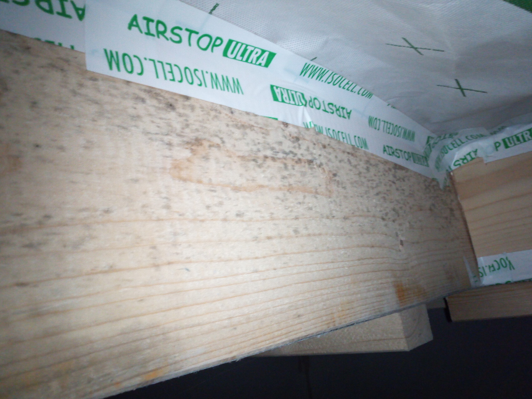 Baustellenansicht: Holzbalken mit grünem AIRSTOP ULTRA-Dichtungsband an Wand und Decke.
